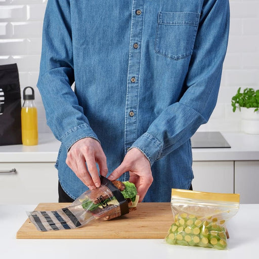 Sandwich being packed into IKEA ISTAD resealable bag on wooden cutting board with grapes nearby