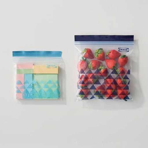 Two IKEA ISTAD blue resealable bags — one storing colourful paper, one filled with fresh strawberries
