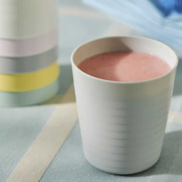 White IKEA KALAS mug with pink liquid next to a colourful stackable cup on striped tablecloth