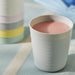 White IKEA KALAS mug with pink liquid next to a colourful stackable cup on striped tablecloth