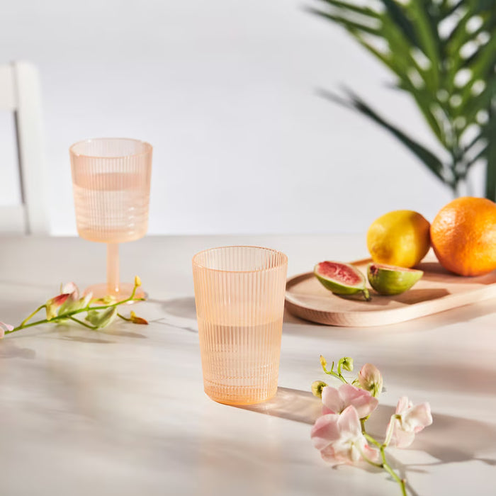  Two IKEA KALLSINNIG plastic glasses styled on a light table with fruits and flowers, outdoor party setting