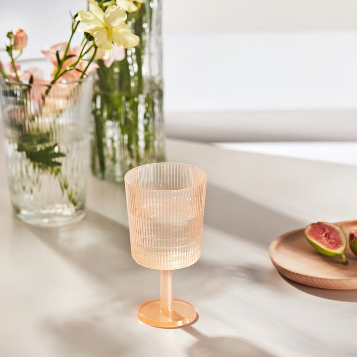 IKEA KALLSINNIG orange plastic wine glass styled outdoors near flower vases on a table