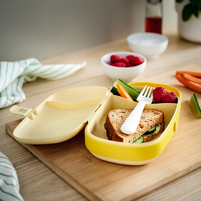 IKEA KAPTENSFISK yellow lunch box open showing sandwich, fruits, vegetables and cutlery slot on wooden surface