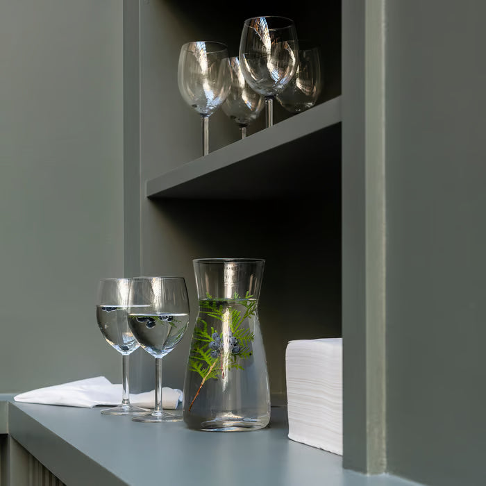 IKEA KARAFF glass carafe with greenery displayed on a grey shelf alongside two wine glasses green backdrop