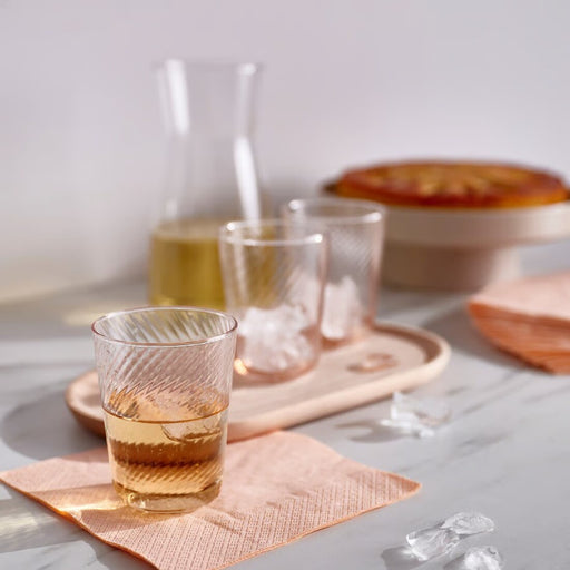 Glass of amber liquid on a pink napkin with a blurred background
