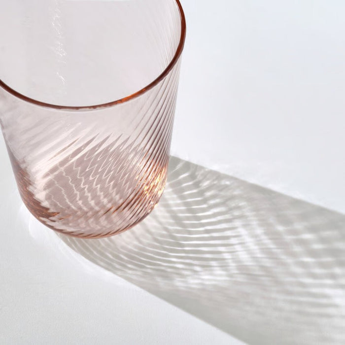 Pink glass tumbler with wavy pattern on a white background