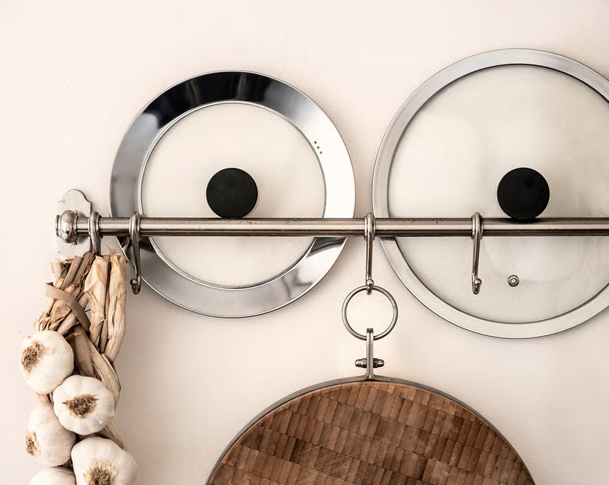 Two IKEA KLOCKREN glass pan lids hanging on kitchen hooks with wooden cutting board below