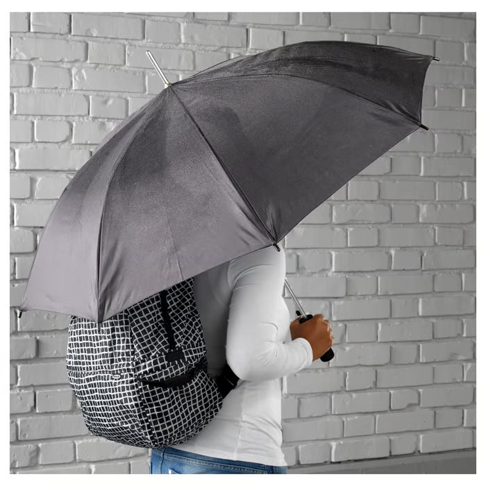 Person holding large black IKEA KNALLA umbrella one-handed in rain providing full coverage