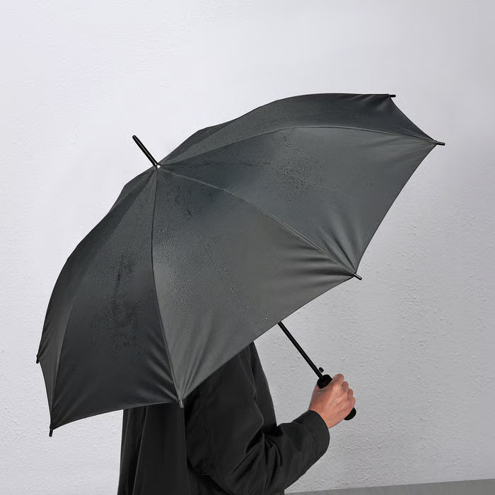 Person holding closed IKEA KNALLA black umbrella indoors showing slim profile and EVA handle