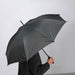 Person holding closed IKEA KNALLA black umbrella indoors showing slim profile and EVA handle