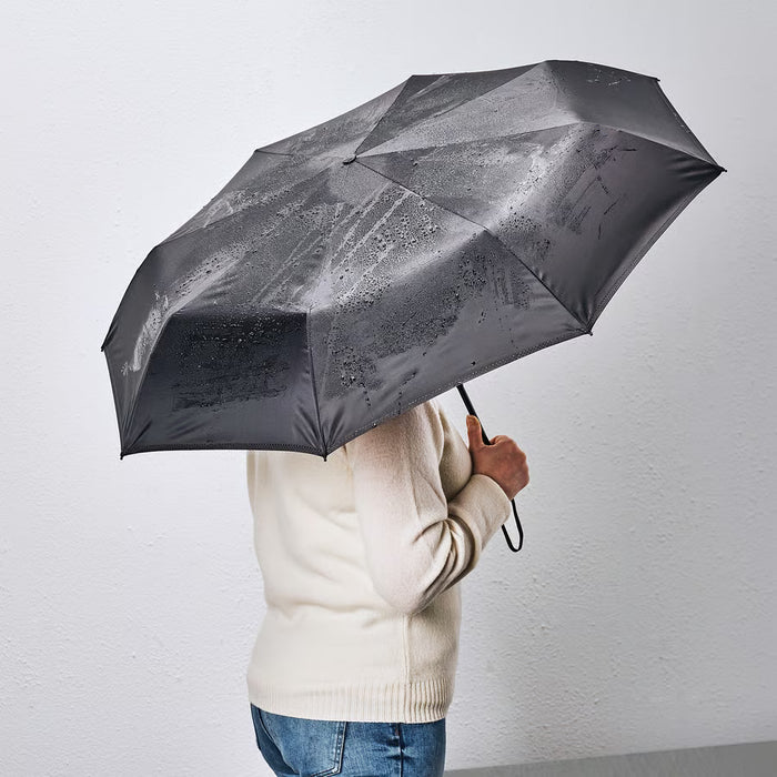 Person holding IKEA KNALLA black foldable umbrella showing wrist strap for easy carrying