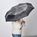 Person holding IKEA KNALLA black foldable umbrella showing wrist strap for easy carrying