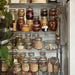 Kitchen shelves displaying IKEA KORKEN jars filled with pickles, jams, and grains in an organised pantry
