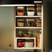 Open cabinet with multiple IKEA KORKEN jars storing dry goods, pickles, and jams in an organised kitchen