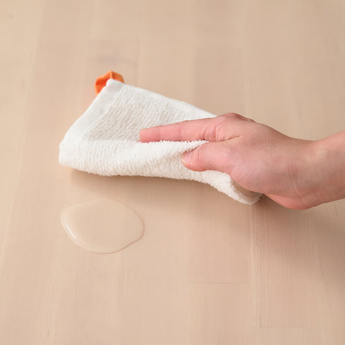Hand wiping wooden surface with IKEA KRAMA white cotton washcloth