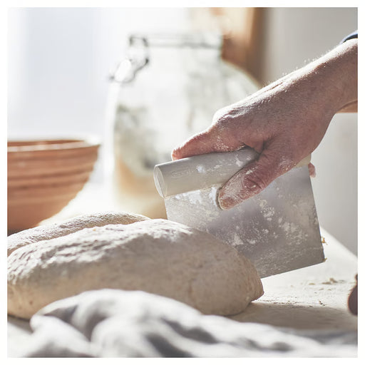 Hand holding IKEA LÄTTBAKAD dough cutter cutting bread loaf with flour on counter
