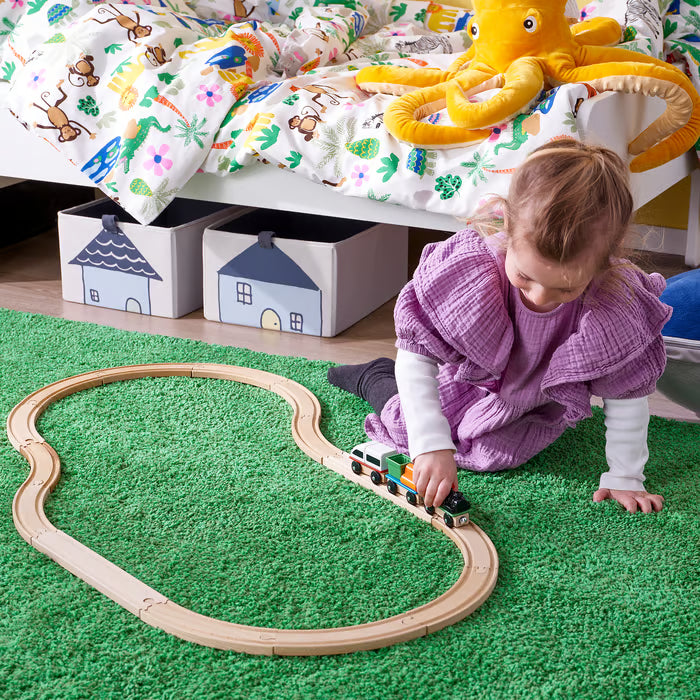Toddler playing with IKEA LILLABO magnetic wooden train set on green rug imaginative floor play