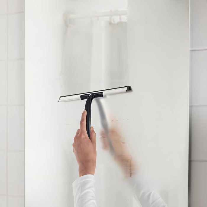Person using IKEA LILLNAGGEN black squeegee to clean glass in a white bathroom