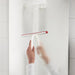 Person cleaning transparent shower glass door with IKEA LILLNAGGEN white and red squeegee