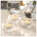 Three lit LÖVSKOGSLUND glass tealights on white surface with blurred vase in background