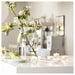 Lit LÖVSKOGSLUND tealights on white counter with glass vase, blooming branches and green apples