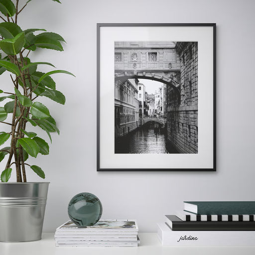 IKEA LOMVIKEN black frame displaying a black and white canal bridge print in a styled living room with plant and books