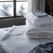 IKEA LUDDROS white quilted mattress protector folded at foot of bed with grey pillow and window view
