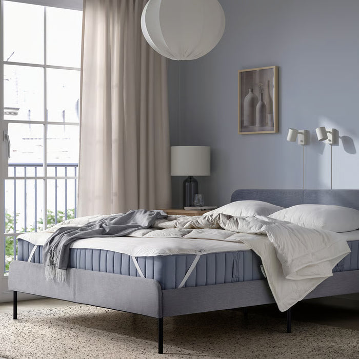 IKEA LUDDROS quilted mattress protector on blue-grey bed in modern bedroom with large window