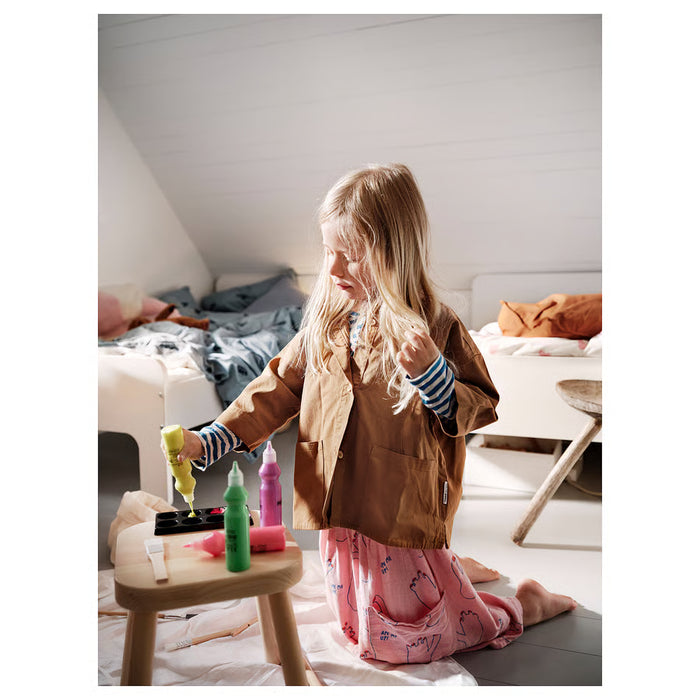 Young girl in yellow apron painting at a wooden easel using IKEA MÅLA brushes with a colour palette