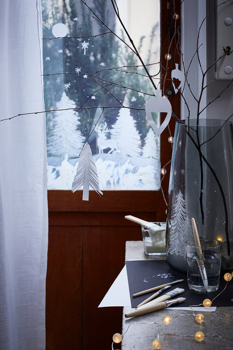 Paper ornaments and bare branches in a vase on a snowy windowsill, decorated using IKEA MÅLA craft supplies