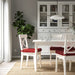 Dining room with white table and chairs with red cushions, large cabinet, and plant.