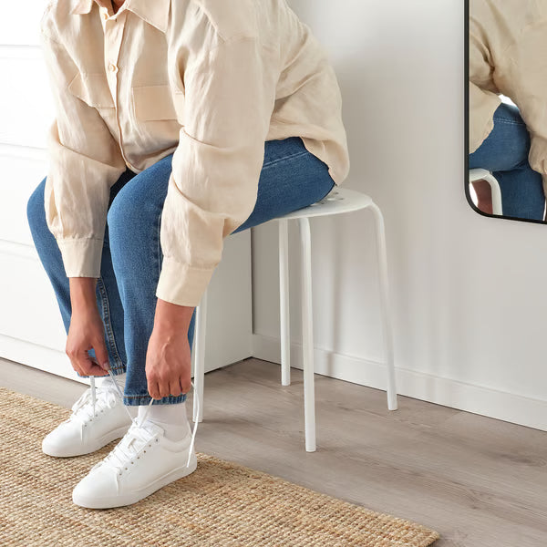  Person tying shoes while seated on IKEA MARIUS white stool showing everyday entryway use
