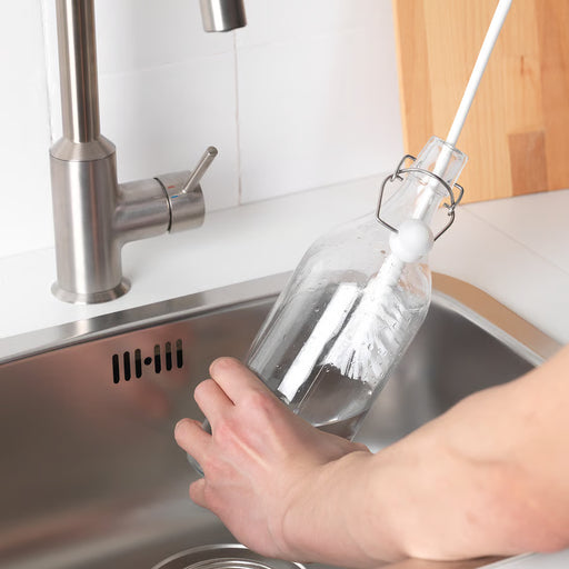  Person using IKEA MEDELVÅG white bottle brush to clean inside a glass bottle at kitchen sink