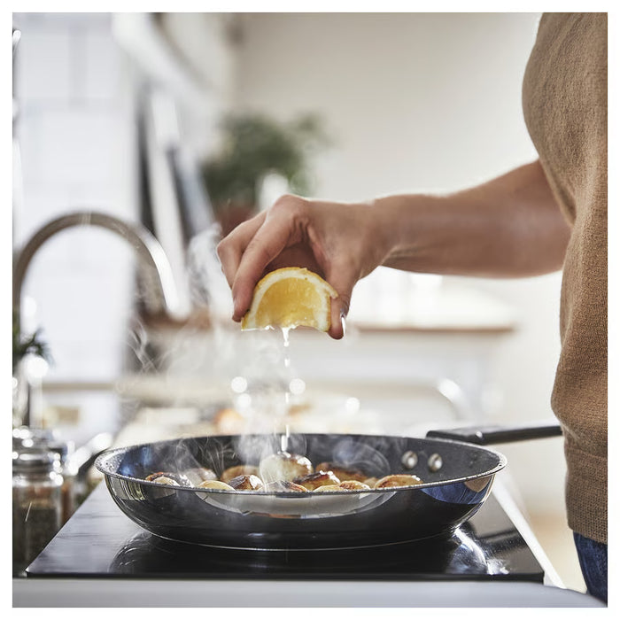 Cooking in IKEA MIDDAGSMAT frying pan, squeezing lemon with steam rising in kitchen setting