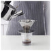 Hand pouring hot water from IKEA ÖVERST metal kettle into stainless steel coffee dripper in use