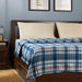 IKEA ODENSLÄTA blue and white check blanket on bed with white pillows and bedside table with lamp