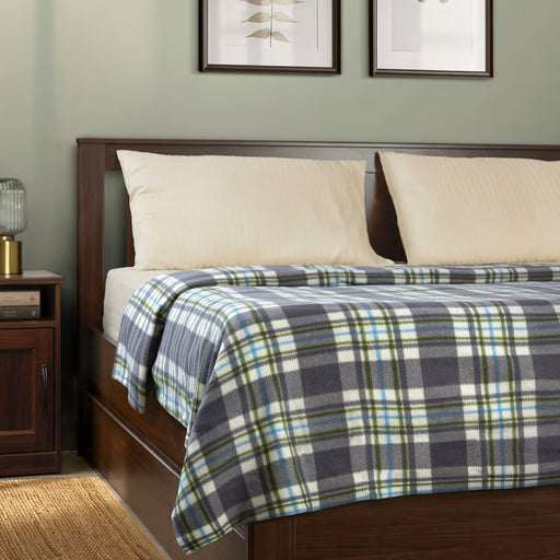 IKEA ODENSLÄTA check blanket in grey and green draped on a bed with pillows and lamp