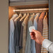 Hand holding a device in front of a wardrobe with hanging clothes