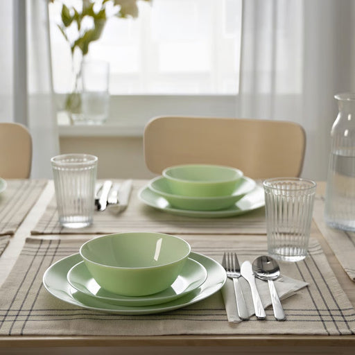 A round, light green ceramic plate with a glossy finish and slightly curved edges, placed against a plain white background."