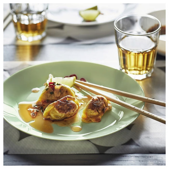 A breakfast spread on a wooden table featuring a green bowl, green plates with a croissant and a slice of cheese, a glass jar of granola, a pitcher of milk, sliced bread on a wooden cutting board, a fork, and a striped cloth napkin, bathed in natural light for a warm and inviting feel."