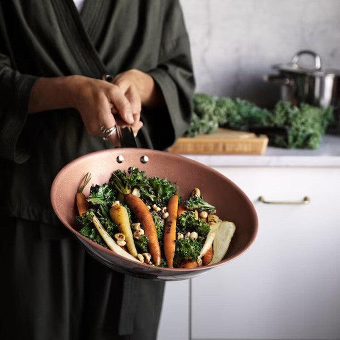 Person holding a pan with a salad of greens and carrots in a kitchen setting