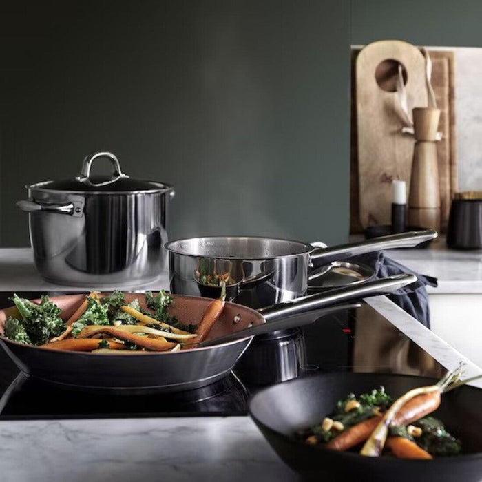 Stainless steel cookware set on a stove with vegetables being cooked.