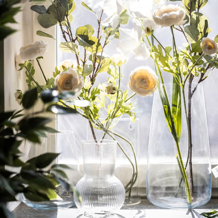 Multiple IKEA PÅDRAG clear glass vases with white flowers and greenery on a window sill