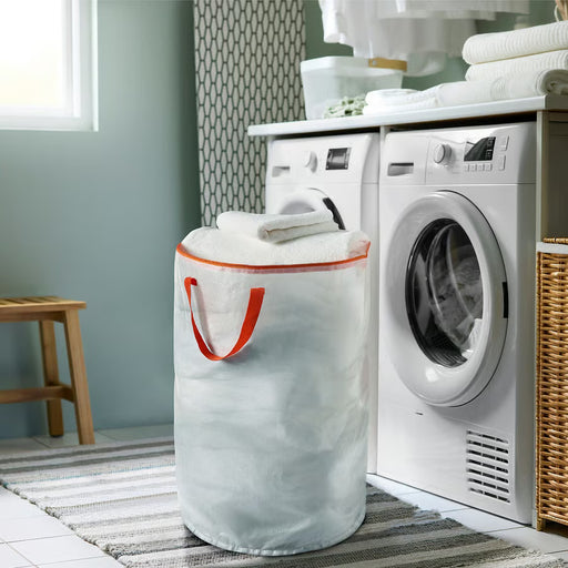 IKEA PÄRKLA white laundry bag with orange handles placed next to washing machine