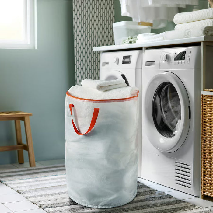 IKEA PÄRKLA white laundry bag with orange handles placed next to washing machine