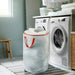 IKEA PÄRKLA white laundry bag with orange handles placed next to washing machine