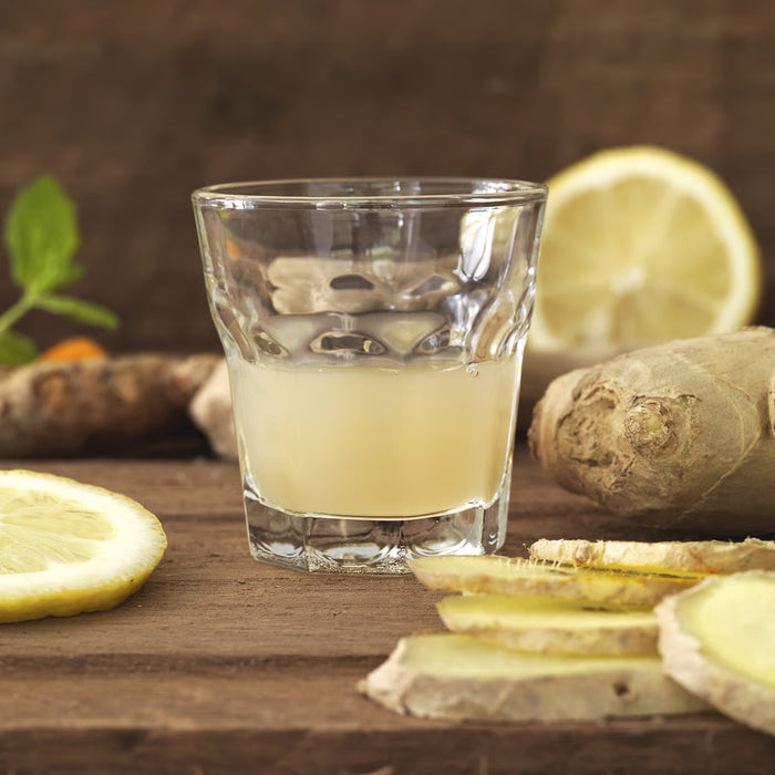 IKEA POKAL clear snaps glass filled with pale yellow drink on wooden surface with lemon and ginger
