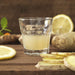 IKEA POKAL clear snaps glass filled with pale yellow drink on wooden surface with lemon and ginger