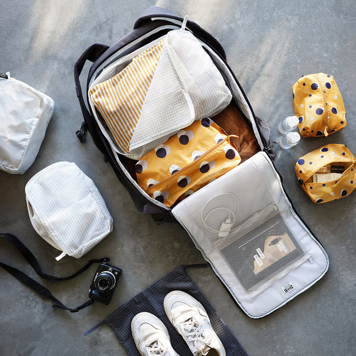 Open backpack with IKEA RENSARE grey check packing cube alongside clothing accessories and shoes