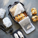 Open backpack with IKEA RENSARE grey check packing cube alongside clothing accessories and shoes